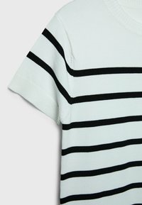 Haut en maille blanc à manches courtes avec des rayures horizontales noires sur la poitrine et la manche, doté d'un col rond.