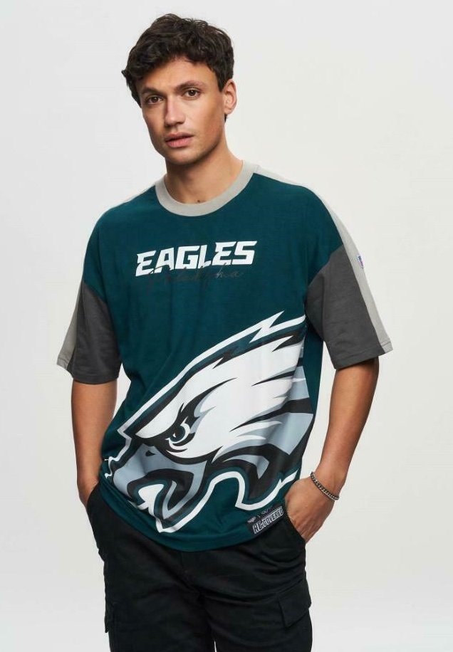 Vihreä ja harmaa ylisuuri T-paita, jossa on suuri kotka-logo ja teksti "EAGLES." Puuvillaa ja lyhythihaista muotoilua.