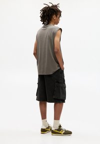 Grijze mouwloze t-shirt, zwarte cargoshorts met zijzakken, witte sokken en groene sneakers met gele accenten. Eenvoudige, casual outfit.