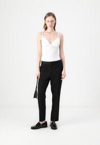 White fitted tank top with thin straps, paired with black straight-legged trousers and black lace-up shoes. Minimalist design, sleek silhouette.