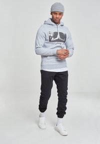 Gray hoodie with graphic print, black pants, and white sneakers. Model wears a knit beanie. Material appears soft with a casual fit.