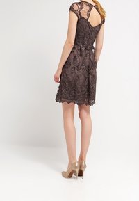 Robe en dentelle marron avec des manches courtes, un dos en V et un ourlet festonné. Dotée de motifs floraux et d'une taille cintrée, accompagnée de talons nude.