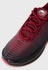 Nike Air Max tenisica s gornjim dijelom u maroon gradijentu, mrežastom teksturom, crnom potplatom, istaknutim vezicama i kružnim logom na jeziku.