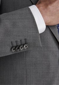 Poignet de veste de costume gris avec quatre boutons noirs, poignet de chemise blanc contrastant en dessous, présentant un tissu texturé et un motif de tissage subtil.