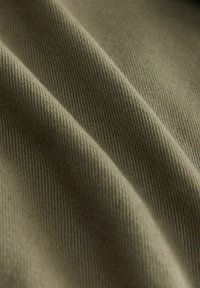 Gros plan sur un tissu vert olive avec une texture visible en sergé diagonal et des plis doux.