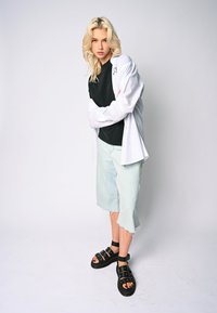 Crna majica ispod bijele oversized košulje, svijetloplave traper šorceve s rupama i crne sandale s remenčićima.