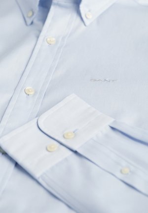 Hele sinine särk, mis on valmistatud kangast, nööpidega krae, valged nööbid, rinnal brod jedis "GANT" logo, sujuv tekstuur.