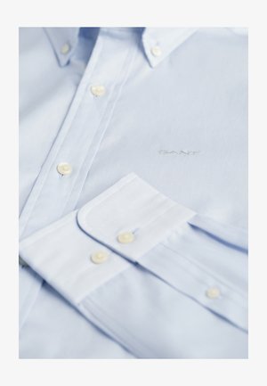 Hele sinine särk, mis on valmistatud kangast, nööpidega krae, valged nööbid, rinnal brod jedis "GANT" logo, sujuv tekstuur.