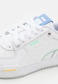 Sneaker bianco in pelle con superficie testurizzata, accenti azzurri e una striscia verde menta. Presenta lacci bianchi e il logo Puma.