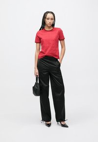 Red short-sleeve t-shirt with a subtle textured pattern, paired with black loose-fitting trousers and black pointed-toe heels. Small black handbag.