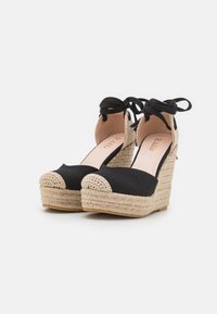 Chaussures à talon compensé en toile noire avec des détails en corde de jute, dos ouvert et lanières à nouer. Bout arrondi avec texture tissée à l'avant.