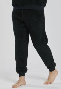 Schwarze Fleece-Jogginghosen mit Rippbündchen und Bund. Weicher, strukturierter Stoff. Kordelzugverschluss an der Taille. Geeignet für Freizeitkleidung.