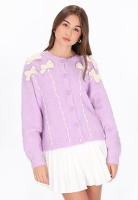 Lavende-farbener gestrickter Cardigan mit cremefarbenen Schleifen und dekorativen Nähten. Er verfügt über einen runden Ausschnitt, lange Ärmel und einen vorderen Knopfverschluss.