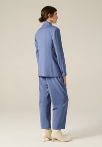 Completo su misura blu chiaro con blazer lungo e pantaloni larghi. Tessuto morbido, design minimalista e dettagli con un solo bottone sul blazer.