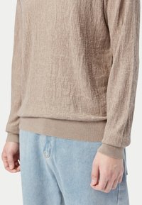 Beige texturerad långärmad skjorta med ribbade muddar och fåll, kombinerad med ljusblåa jeans i denim.