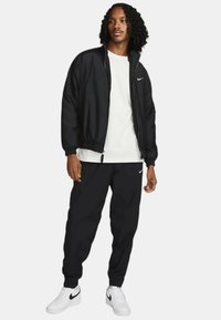 Svart Nike zip-up jacka och svarta sweatpants, kombinerat med en vit t-shirt och vita sneakers med svarta accenter.