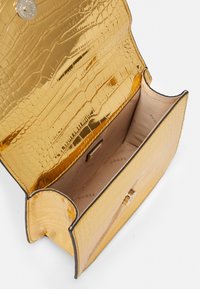 Gylden faux krokodilleder skuldertaske med en glitrende finish, der har en enkelt lås og en glat beige indvendig foring.