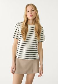 Gestreept T-shirt in crème en zwart met korte mouwen en een ronde hals, gecombineerd met een beige rok. Gladde stof, casual pasvorm.