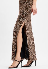 Robe maxi à imprimé léopard avec fente haute, design ajusté, texture lisse et garniture noire. Assortie à des escarpins noirs à lanières.