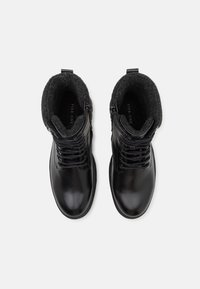 Botas de tobillo de cuero negro con un acabado suave, que cuentan con un forro de fieltro gris suave, cordones en la parte delantera y cremallera lateral para facilitar su uso.