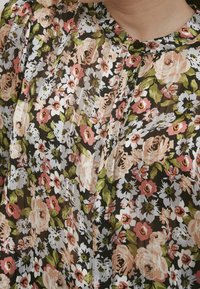Blusa floreale realizzata in tessuto leggero con uno sfondo nero. Presenta fiori rosa, bianchi e verdi, con pieghe e un collo con bottoni.