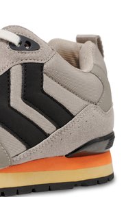 Gray sneaker featuring a suede and mesh upper, black chevron accents, and a multicolored sole with orange and yellow details.