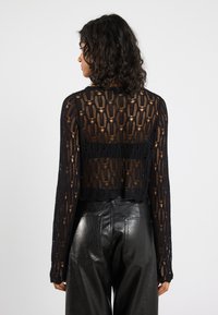 Maglione corto nero realizzato in tessuto a maglia aperta con motivo floreale. Maniche lunghe, scollatura rotonda e pantaloni in pelle nera testurizzati.