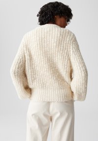 Maglione lavorato a maglia spesso di colore bianco sporco, caratterizzato da un motivo testurizzato e maniche ampie e larghe. L'orlo a coste offre un finish aderente.