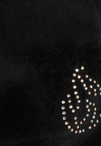 Un tissu noir présentant une texture douce avec un motif de strass colorés disposés en une forme fluide à la surface.