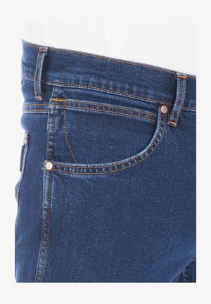 Niebieskie dżinsy o wąskim kroju, miedzianym przeszyciu i małej przedniej kieszeni. Materiał ma gładką teksturę z delikatnym połyskiem.