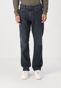 Mørkeblå denimjeans med rett passform, fem lommer og lett falming. Kombinert med hvite sneakers på en enkel bakgrunn.