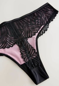 Black lace thong with intricate floral pattern on a soft pink base. Features scalloped edges and a smooth waistband, highlighting contrasting textures.