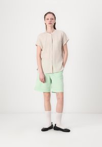Camicia a maniche corte a righe, leggera, abbinata a pantaloni corti verde menta. L'outfit è completato da ballerine nere e calze bianche.