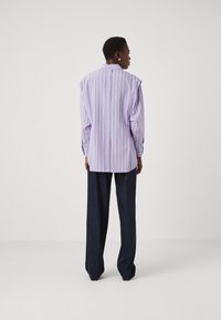 Purple striped oversized shirt with shoulder padding, long sleeves, button cuffs, and a straight hem, paired with dark blue tailored pants.