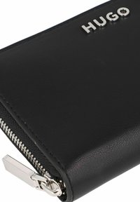 Cartera de cuero negro con el logo plateado "HUGO", textura suave y cierre de cremallera metálica con detalle de acento.