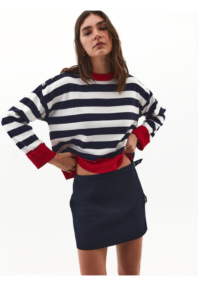 Maglione a righe blu navy e bianco con accenti rossi, caratterizzato da un colletto e polsini a coste, abbinato a una gonna mini blu navy semplice.