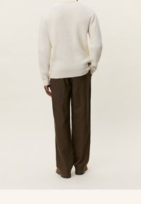 Pull côtelé crème avec un col rond, associé à un pantalon ample marron à carreaux, présentant une coupe décontractée et des textures subtiles.