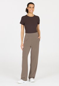 Brown ribbed short-sleeve top paired with high-waisted, loose-fitting beige trousers. The model stands in white athletic shoes.