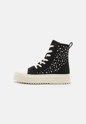 Czarny sneaker za kostkę z białą grubą podeszwą, białymi sznurowadłami i srebrnymi ćwiekami zdobiącymi boczną panel i tył.