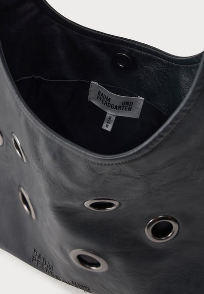 Μαύρη δερμάτινη γυναικεία τσάντα με ασημένιους μεταλλικούς κρίκους, ανοιχτό πάνω μέρος που δείχνει εσωτερική ετικέτα "Baum und Pferdgarten" και κλείσιμο με κουμπί τύπου snap.