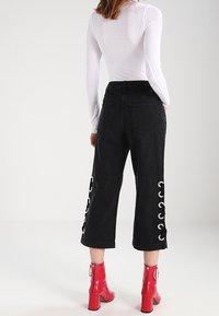 Svarta cropped-byxor med sidogrommet-snörning, tillverkade av denim. Matchad med klarröda högklackade stövlar.