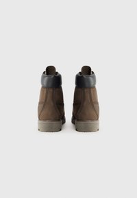 Bottes mi-mollet en cuir marron avec un col rembourré en bleu marine, surface texturée et une semelle en caoutchouc gris robuste. Détails de couture contrastés.