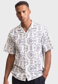 Short-sleeve, button-up shirt made of lightweight fabric with a white base and black geometric patterns throughout. Features a classic collar.