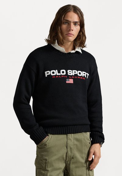 Un pull en tricot noir avec "POLO SPORT" et "RALPH LAUREN" en blanc et rouge, agrémenté d'un accent de drapeau américain. Poignets et ourlet côtelés.
