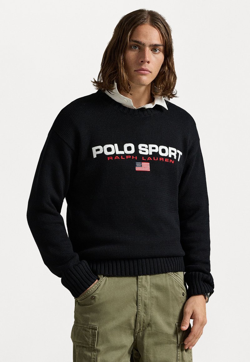 Črna pletena jopica z bele in rdeče napisano "POLO SPORT" in "RALPH LAUREN", z dodatkom ameriške zastave. Ribočasti manšeti in rob.