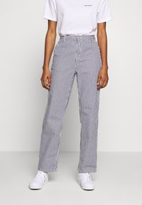 Spodnie w paski z mieszanki bawełny, o luźnym kroju, z wysokim stanem i pionowymi granatowo-białymi paskami. Noszone z białymi trampkami.