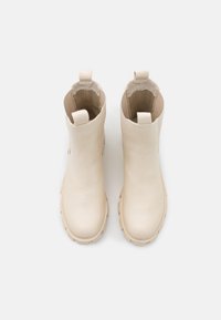 Bottes cheville en cuir beige avec une texture lisse, un bout arrondi et une semelle en caoutchouc dotée d'une adhérence texturée. Comprend des languettes pour un enfilage facile.