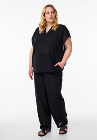 Completo in lino nero, loose-fitting, composto da una parte superiore a maniche corte con scollo a V e pantaloni larghi. Sandali con dettagli a borchie.
