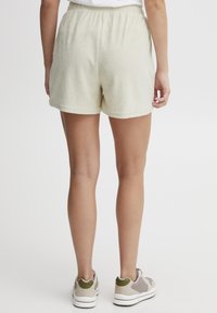 Shorts en éponge jaune clair avec une taille élastique, présentant une coupe décontractée et une texture subtile. Portés avec des baskets de teintes neutres.