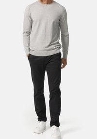 Maglione grigio lavorato a maglia con collo rotondo e polsini a costine, abbinato a pantaloni neri e scarpe da ginnastica bianche. L'outfit è casual e minimalista.